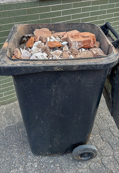 Eine Restmülltonne randvoll gefüllt mit Bauschutt