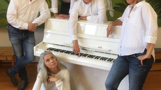 Mitglieder der Band an einem weißen Klavier