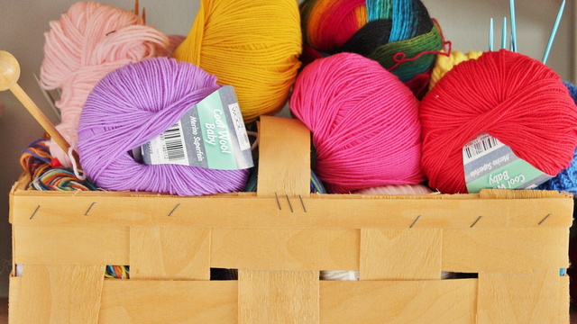 Korb mit bunten Wollknäuelen und Stricknadeln