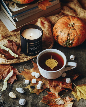 Eine Tasse Tee neben einer Kerze mit Herbstdeko im Hintergrund