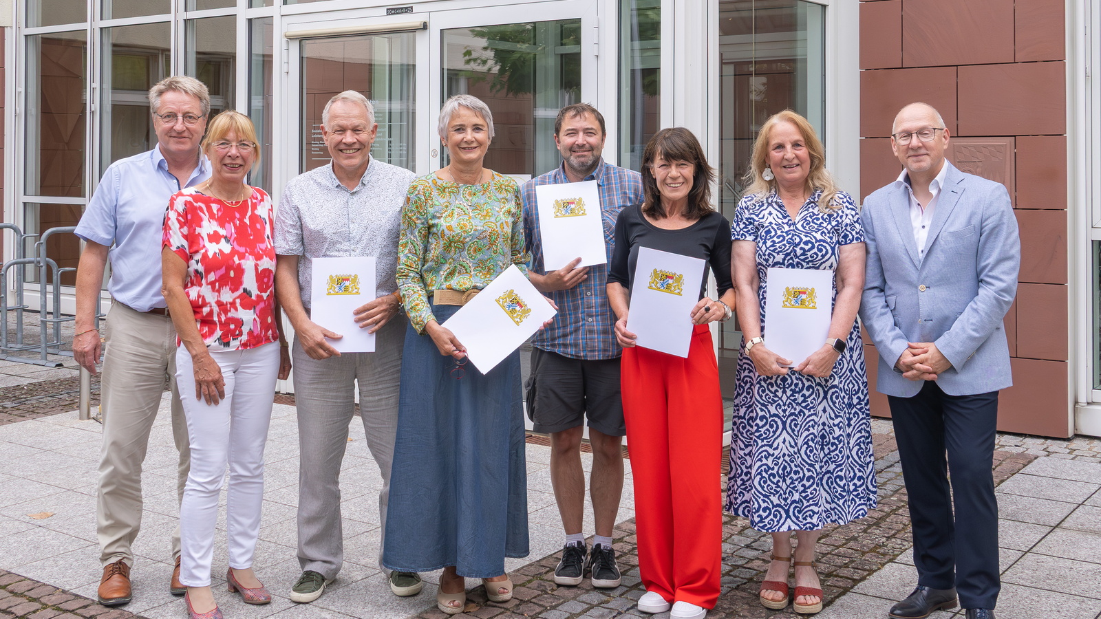 acht Personen mit einer Urkunde in der Hand vor dem Eingang des Landratsamtes