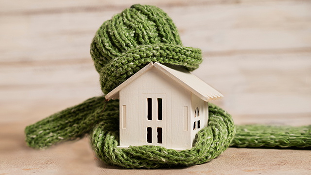Ein symbolisches Haus aus Holz in einer Mütze und Schal eingepackt