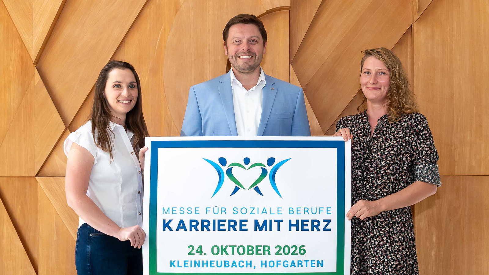 Drei Menschen halten ein Plakat zur Veranstaltung hoch