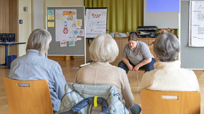 Anleiterin Stefanija Pänkert zeigt den Kutschersitz vor den Teilnehmenden, der bei einem Asthmaanfall akute Atemnot lindern kann.