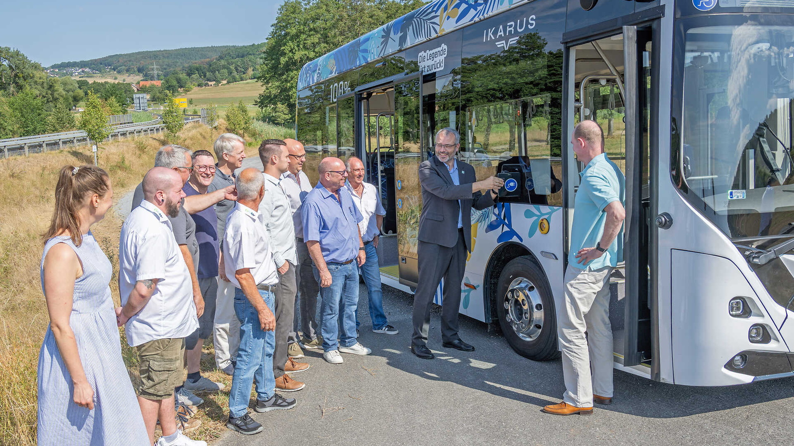 Teilnehmende stehen auf einem Parkplatz vor einem Elektrobus und lassen sich diesen zeigen