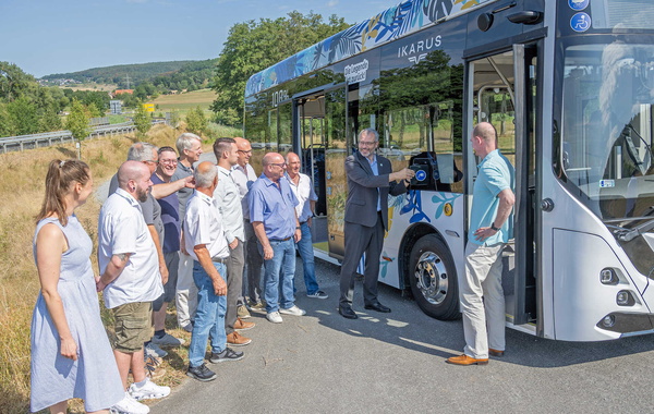 Teilnehmende stehen auf einem Parkplatz vor einem Elektrobus und lassen sich diesen zeigen