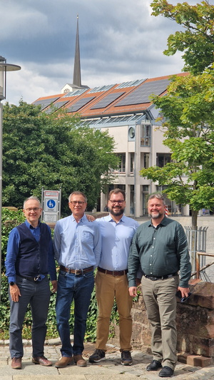 Vier Personen im Hintergrund ein Haus mit Solaranlage
